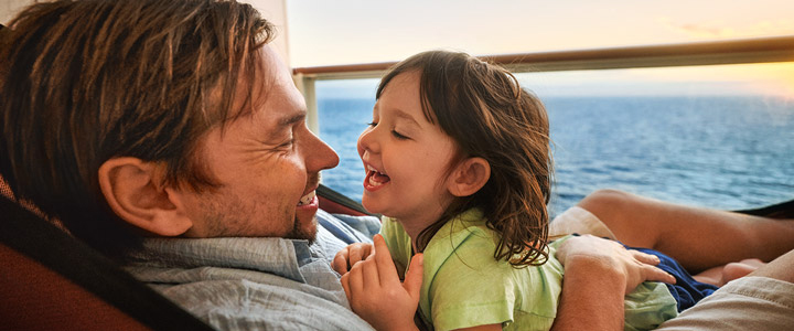 Auf einem Kreuzfahrtschiff liegt ein Kind auf seinem Vater, beide lächeln sich an.